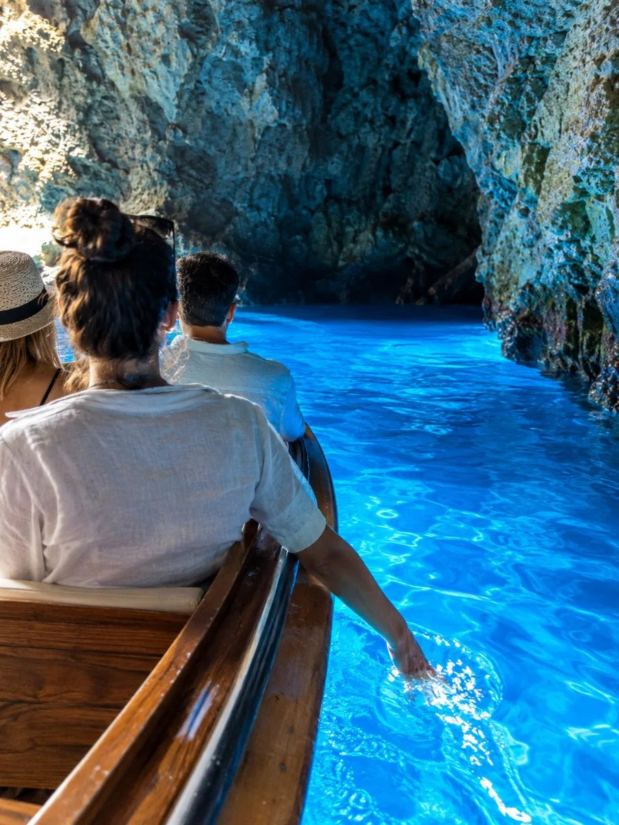 Visitantes en una pequeña barca de madera dentro de la Cueva Azul, con el agua brillando en azul bajo ellos